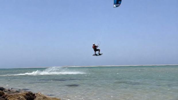 A kitesurfer airborne above a shallow turquoise lagoon.
