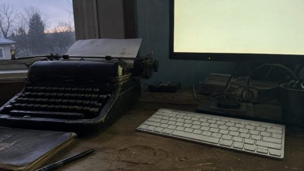 A typewriter and a keyboard side by side on a desk at dusk.