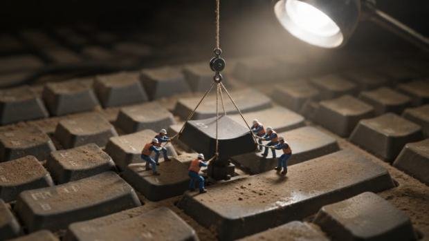Miniature workers lifting a keyboard key with a crane.